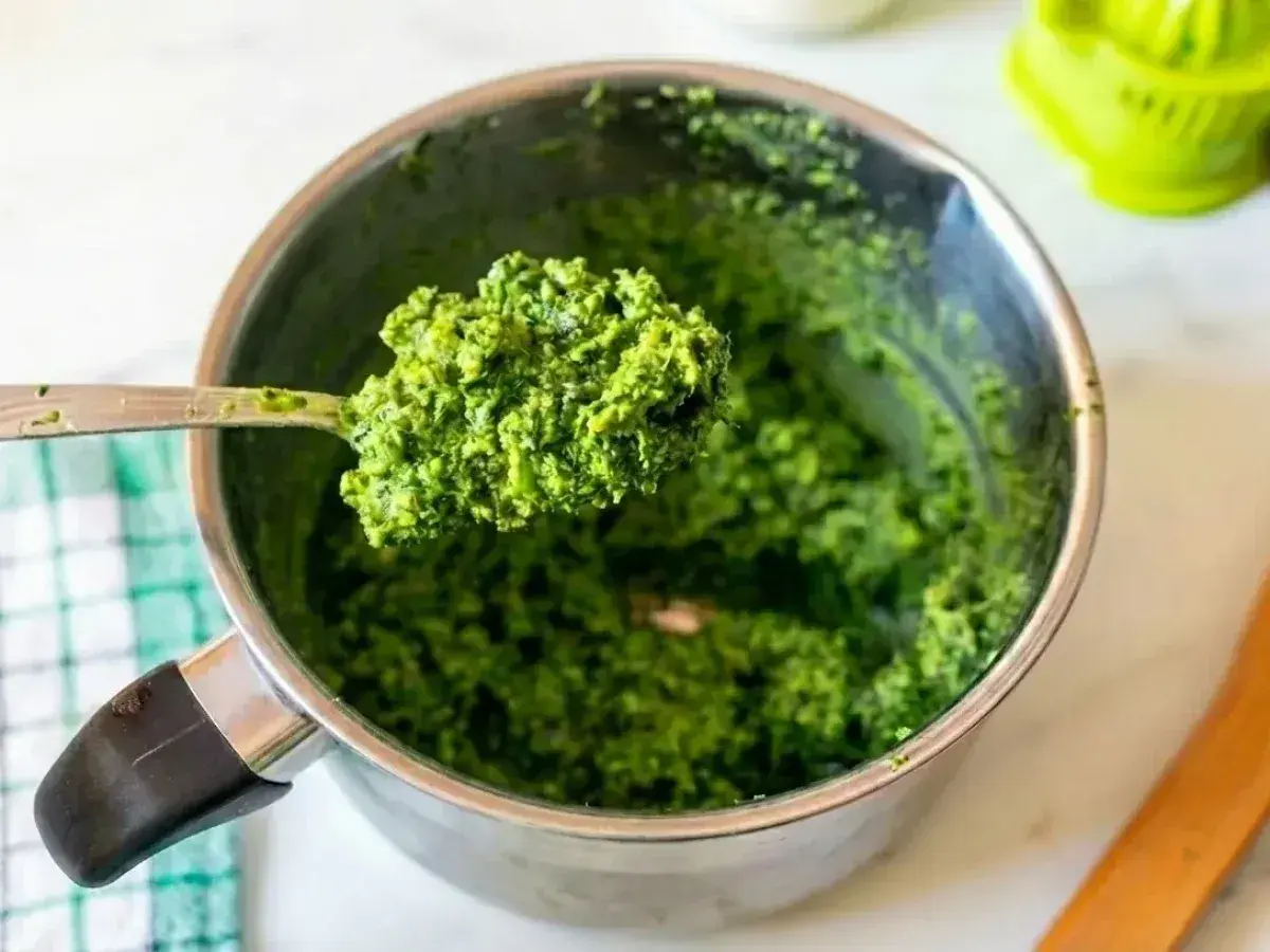 Łyżka świeżego, zielonego pesto bazyliowego nad metalowym garnkiem. Idealne do makaronu!