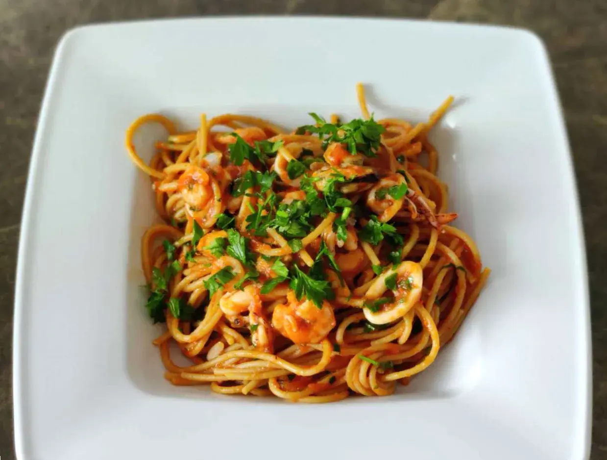 Pyszne spaghetti z owocami morza, krewetkami i kalmarami, posypane świeżą natką pietruszki.