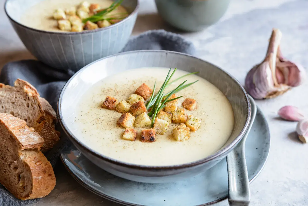 Aksamitna zupa czosnkowa z grzankami i szczypiorkiem, podana z chlebem i czosnkiem.