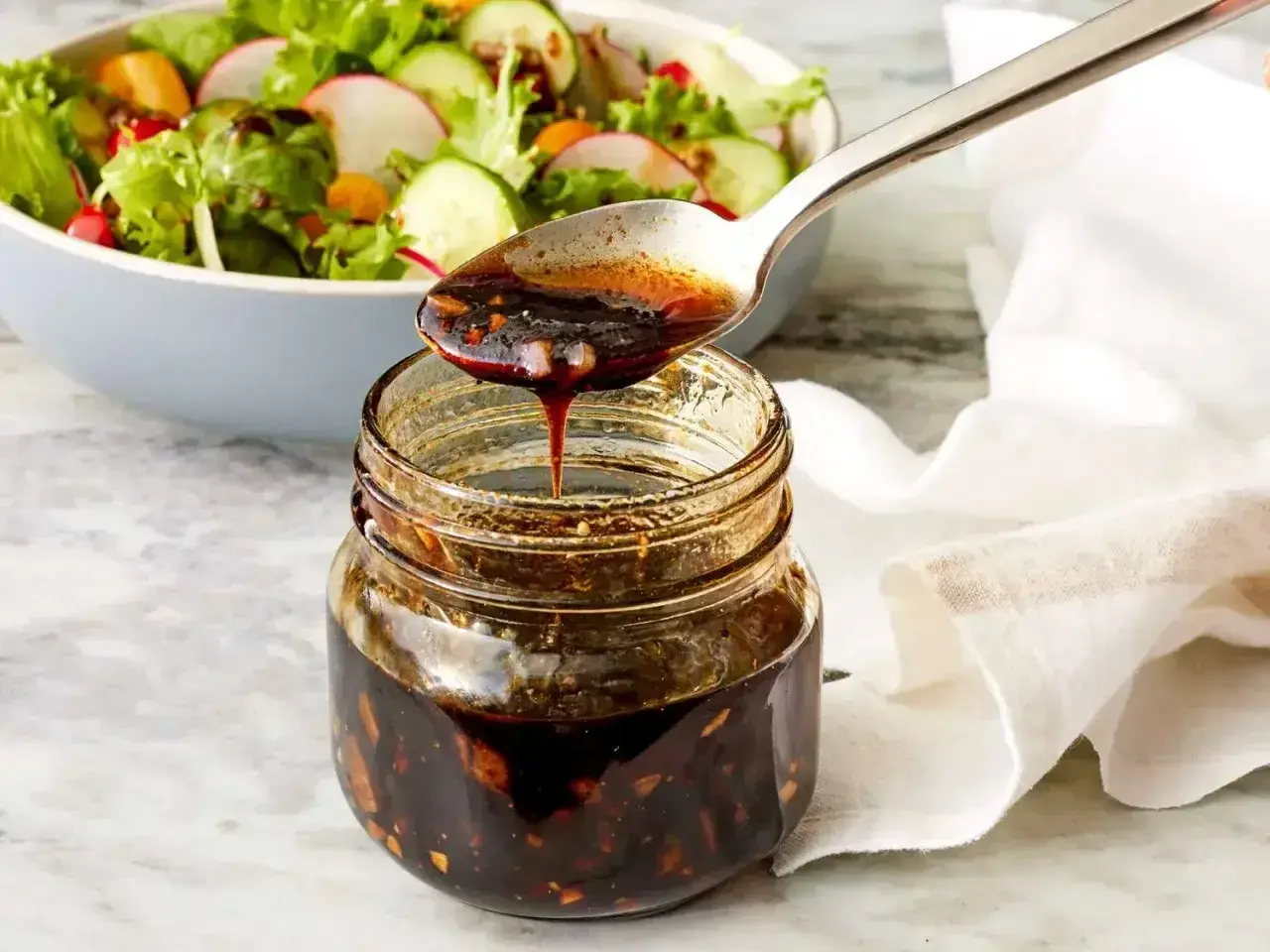 Łyżka polewa sałatkę gęstym, ciemnym sosem balsamicznym z słoiczka.