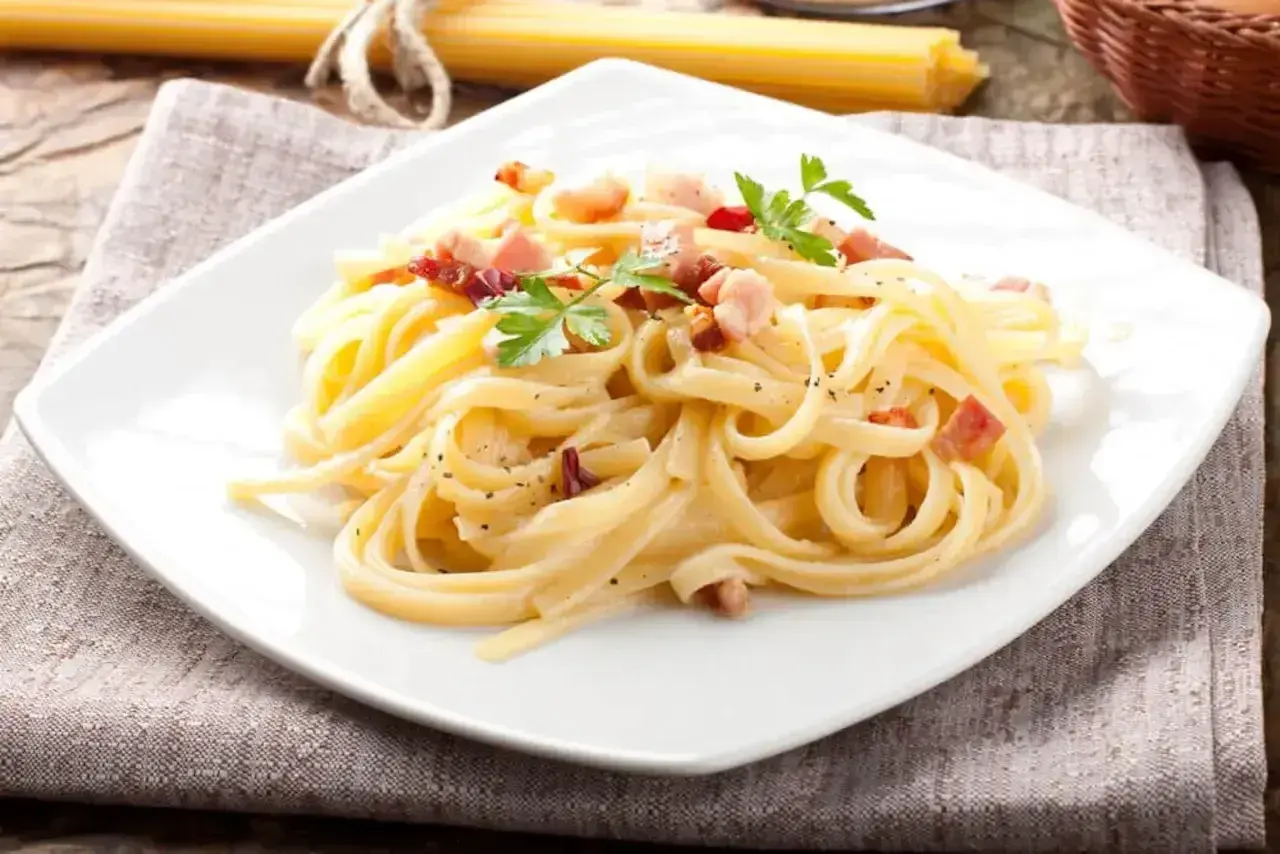 Pyszna carbonara włoska na białym talerzu, udekorowana natką pietruszki i posypana pieprzem.