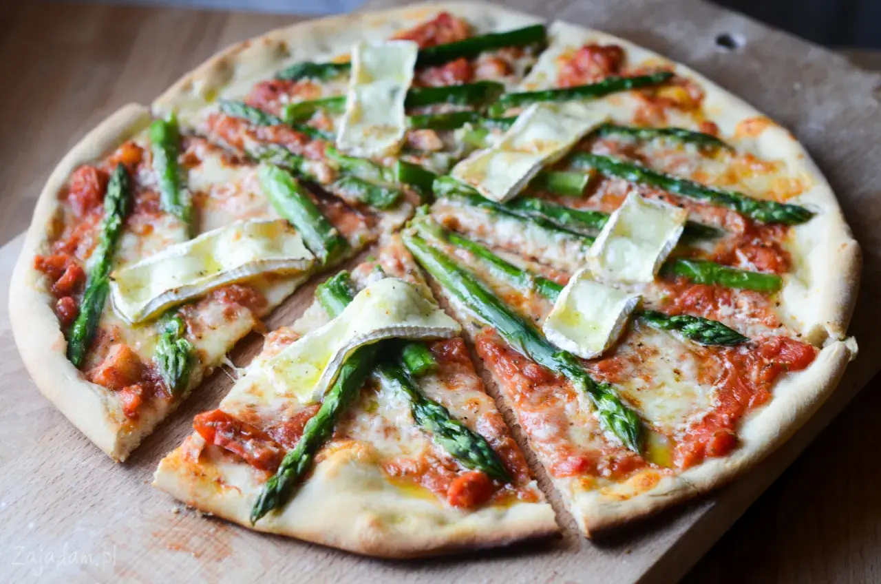Pyszna pizza ze szparagami i serem brie, pokrojona na kawałki, prezentuje się apetycznie na drewnianej desce.