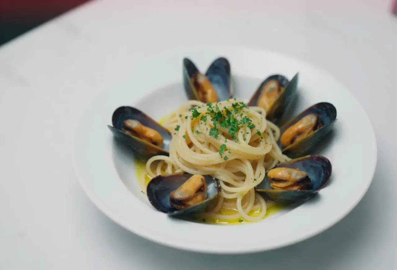 Spaghetti z małżami, danie pełne smaku morza, ozdobione świeżą natką pietruszki.