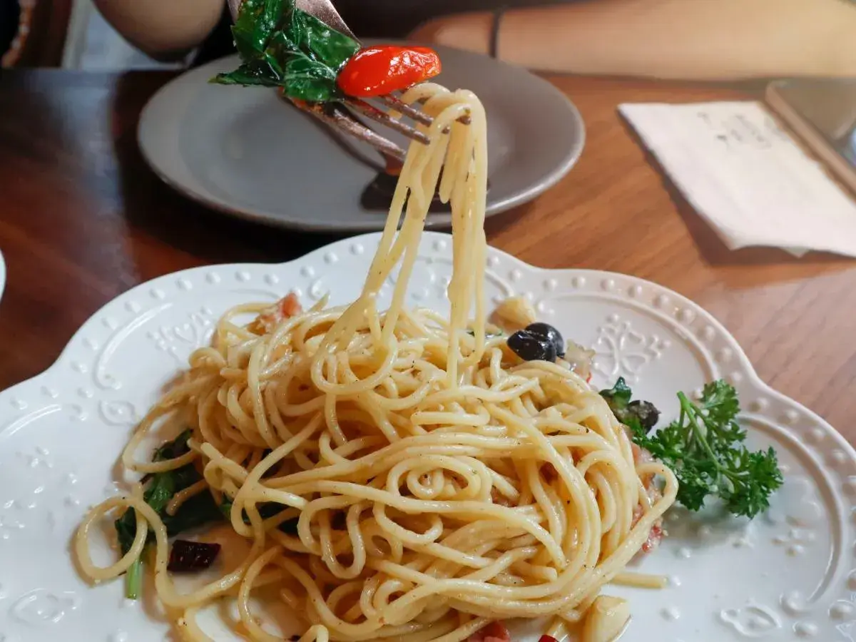 Widok z bliska na talerz pysznego spaghetti aglio e olio, z widelcem unoszącym porcję makaronu z bazylią i pomidorkiem.