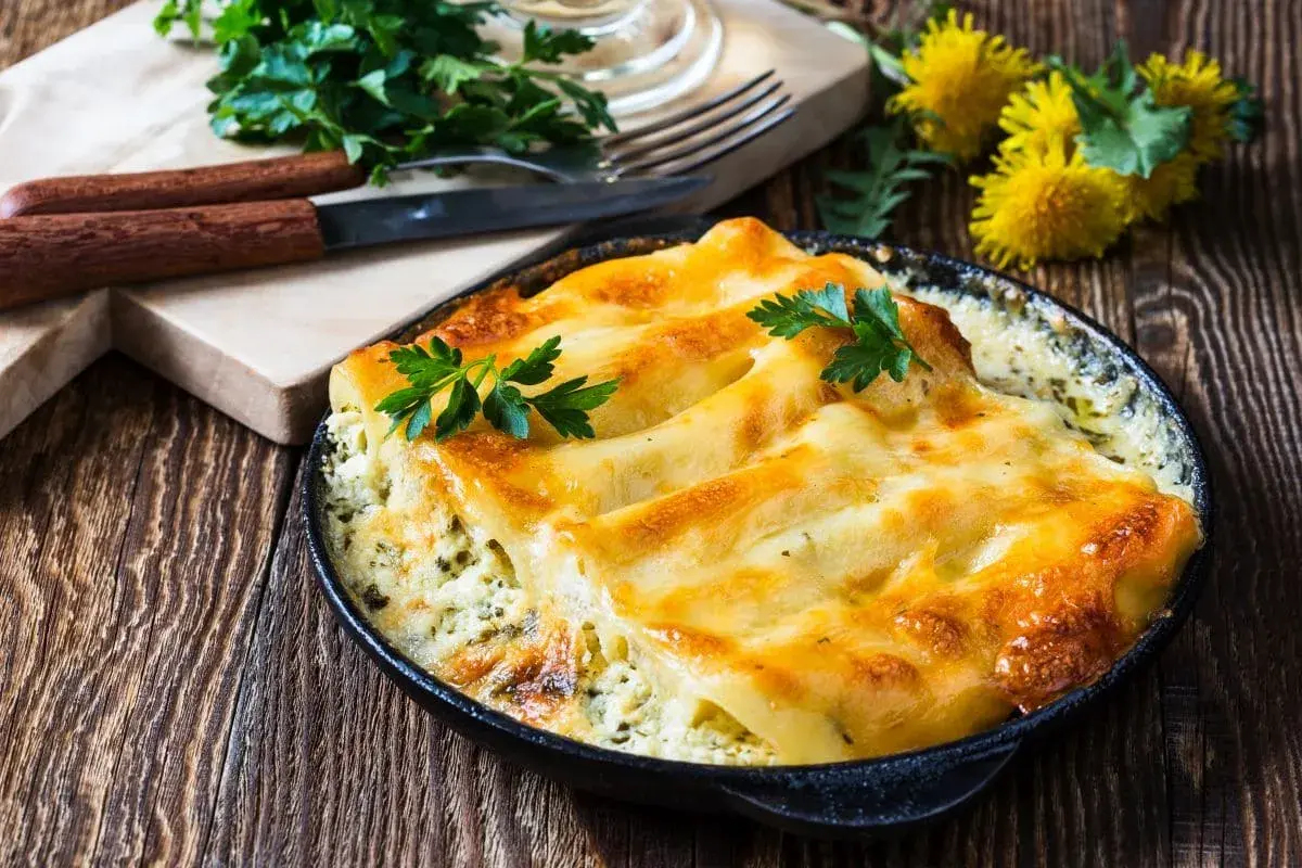 Zapiekane cannelloni w sosie, posypane serem i udekorowane natką pietruszki. Idealne danie na obiad.
