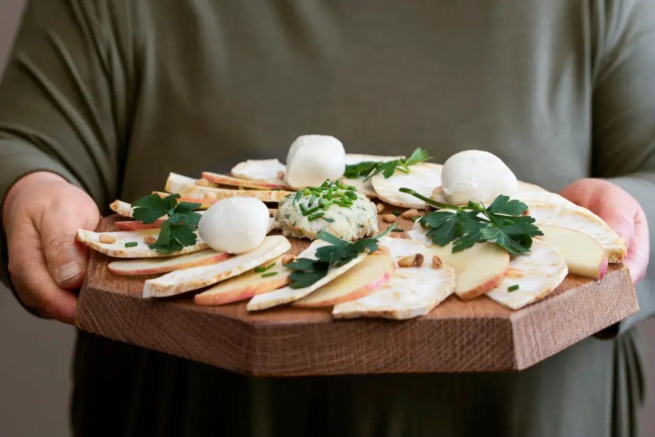 Carpaccio z selera z kulkami mozzarelli, jabłkiem i pastą ziołową na drewnianej desce.