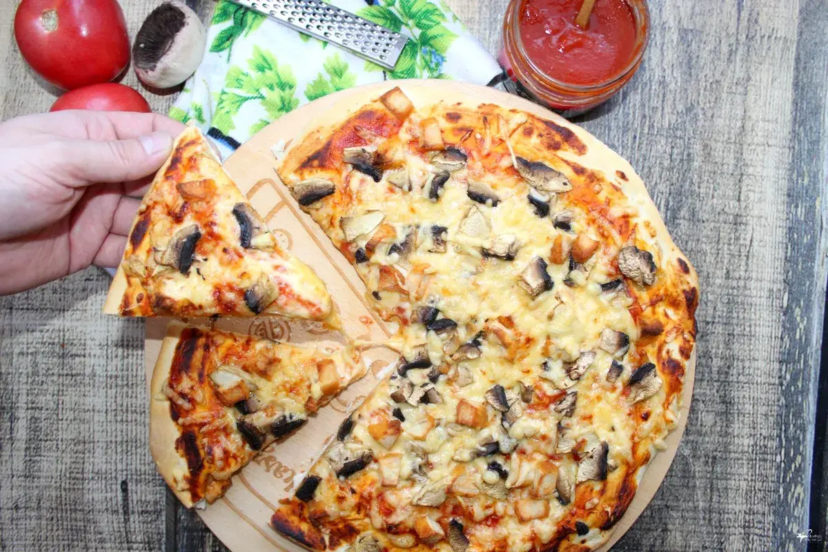 Pyszna pizza domowa z pieczarkami i kurczakiem, właśnie wyjęta z pieca. Ktoś właśnie bierze pierwszy kawałek.