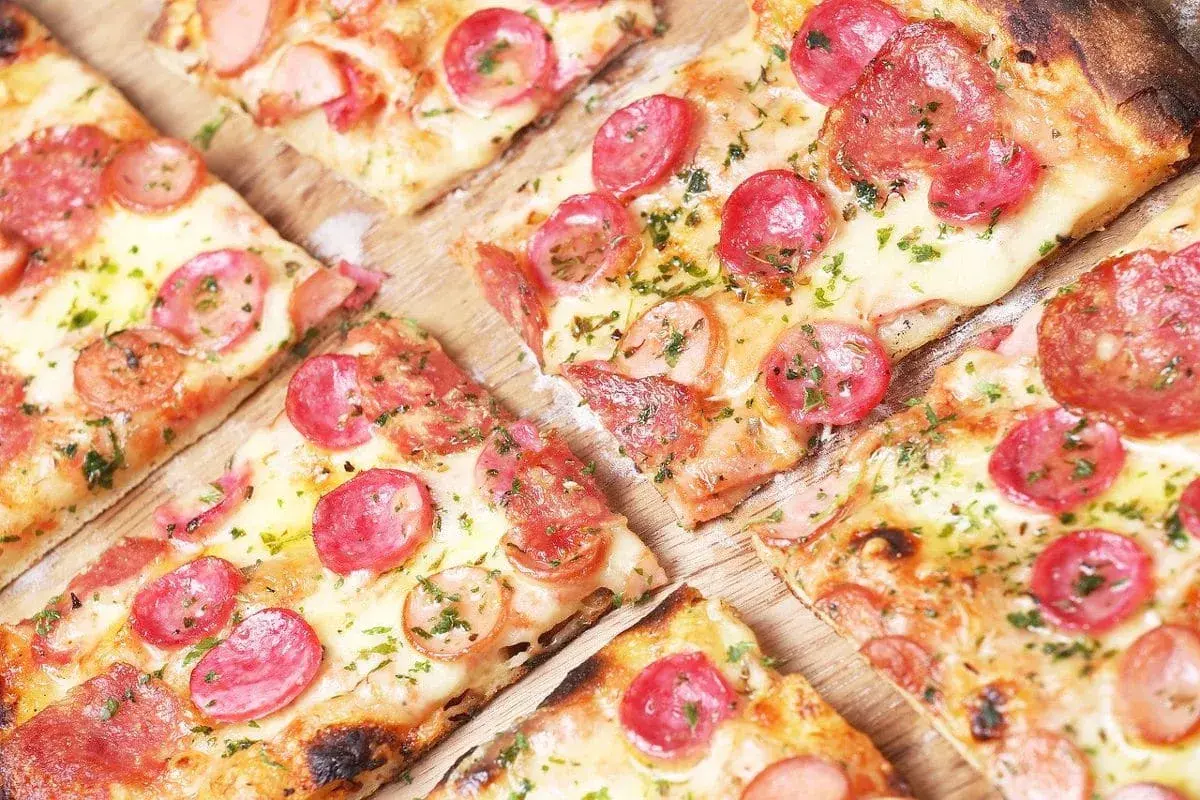 Kawałki pysznej, gorącej pizza włoska z kiełbasą i serem, posypane ziołami. Idealna na spotkanie z przyjaciółmi.