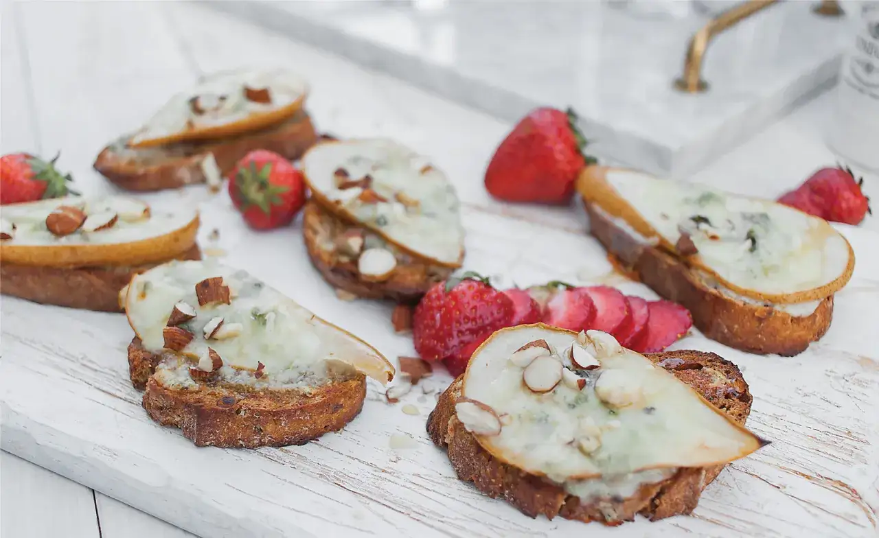 Bruschetta z gorgonzolą, gruszką i migdałami, ozdobiona świeżymi truskawkami. Pyszna przekąska.