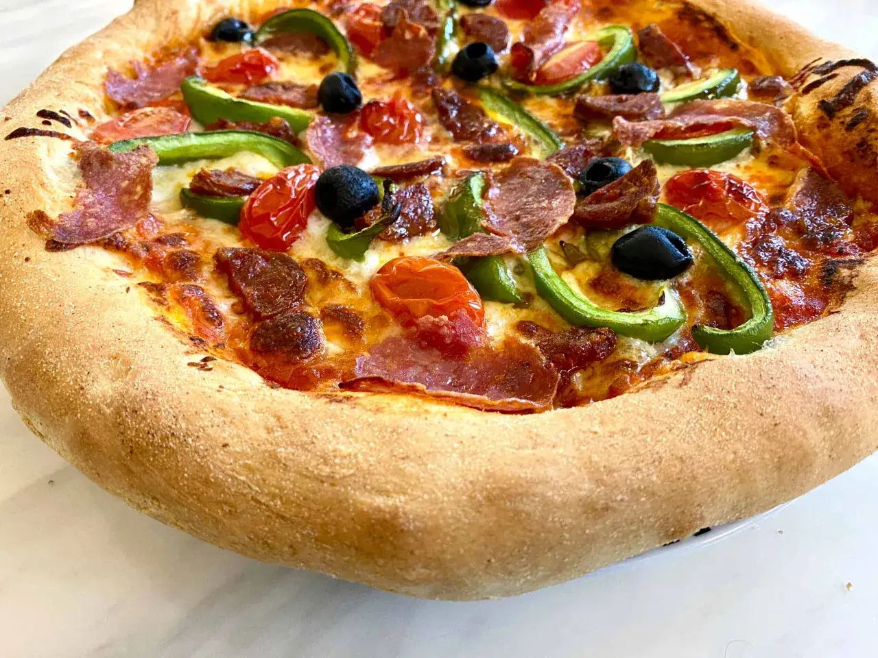 Pyszna pizza z semoliny z pikantnym salami, zieloną papryką, pomidorkami i czarnymi oliwkami.