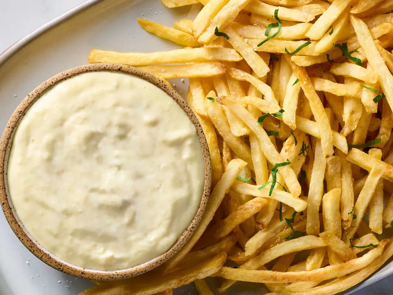 Chrupiące frytki posypane ziołami i solą, obok miseczka kremowego sosu aioli. Idealny duet na przekąskę.