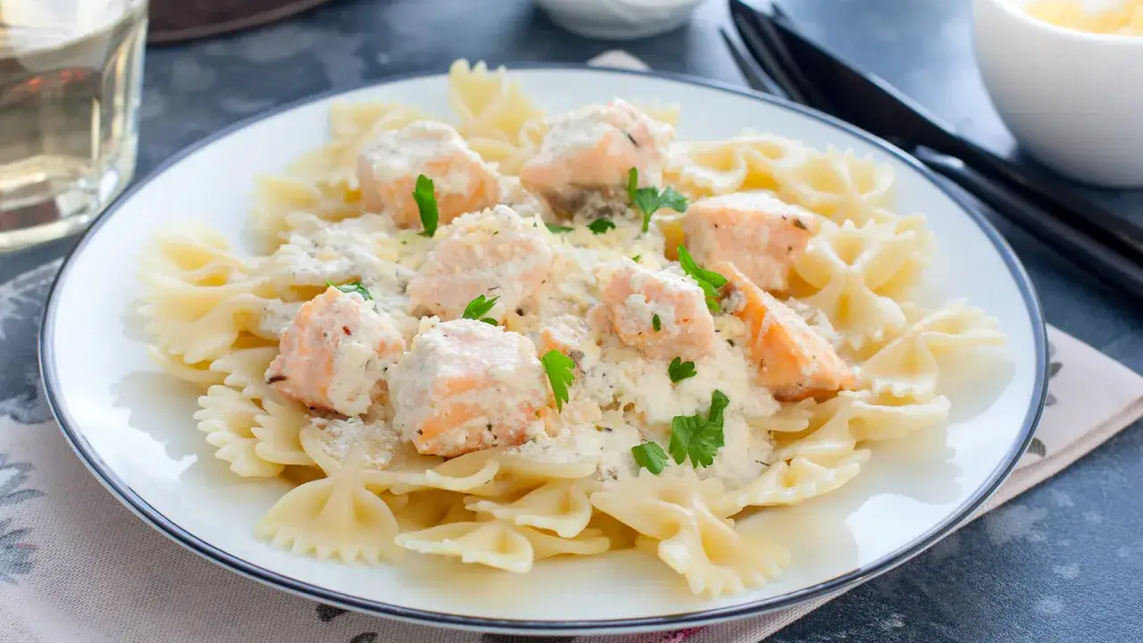 Makaron farfalle z kawałkami łososia w kremowym sosie śmietanowym, udekorowany natką pietruszki. Pyszny sos śmietanowy do łososia.
