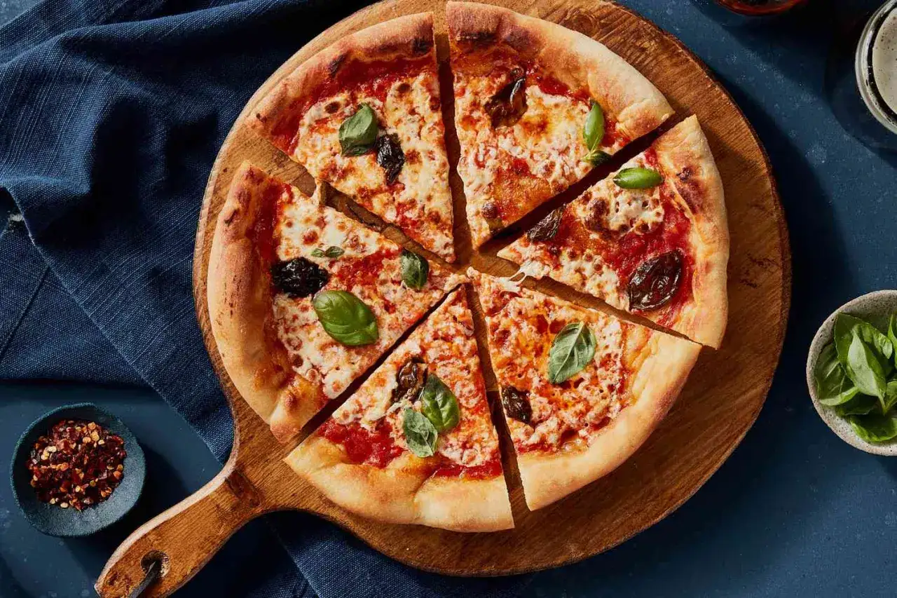 Pyszna pizza margherita z bazylią i pomidorami, pokrojona na kawałki, na drewnianej desce.