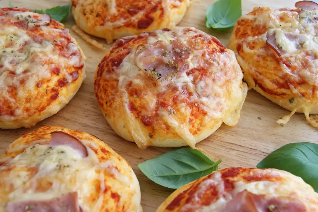 Pyszne, domowe bułeczki pizzowe z serem i szynką, ozdobione listkami bazylii, kuszą apetycznym wyglądem.