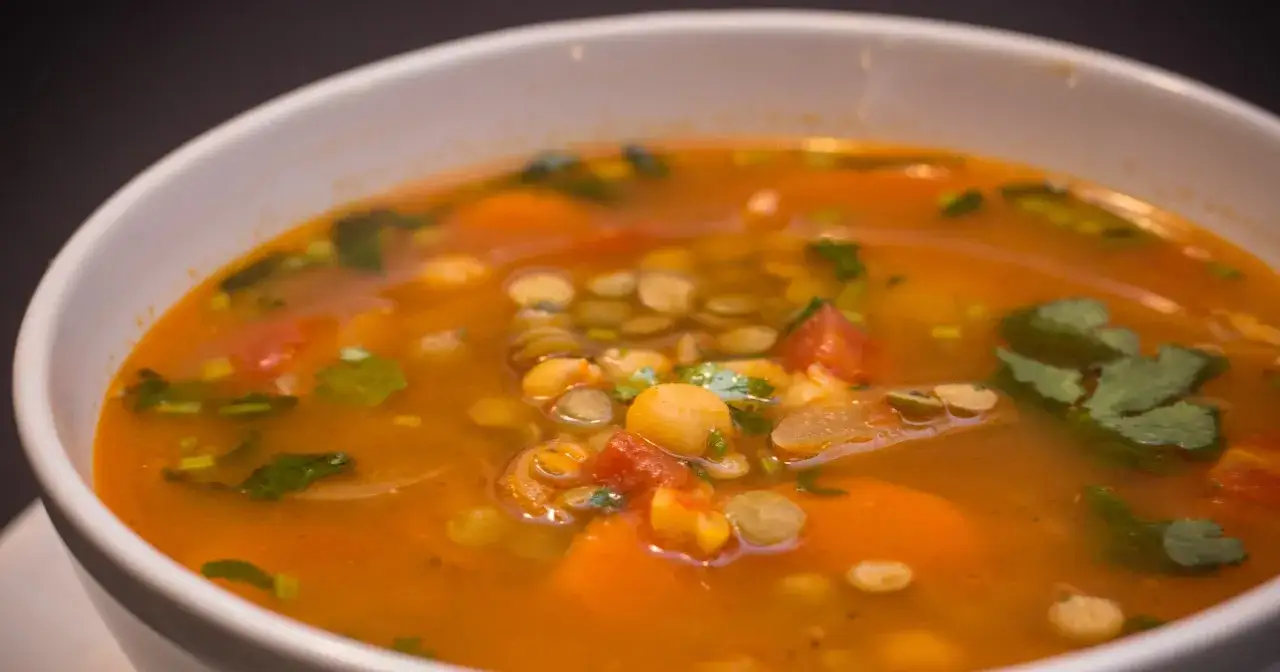 Aromaticzna zupa z ciecierzycy z kawałkami pomidorów i marchewki, ozdobiona świeżą kolendrą.
