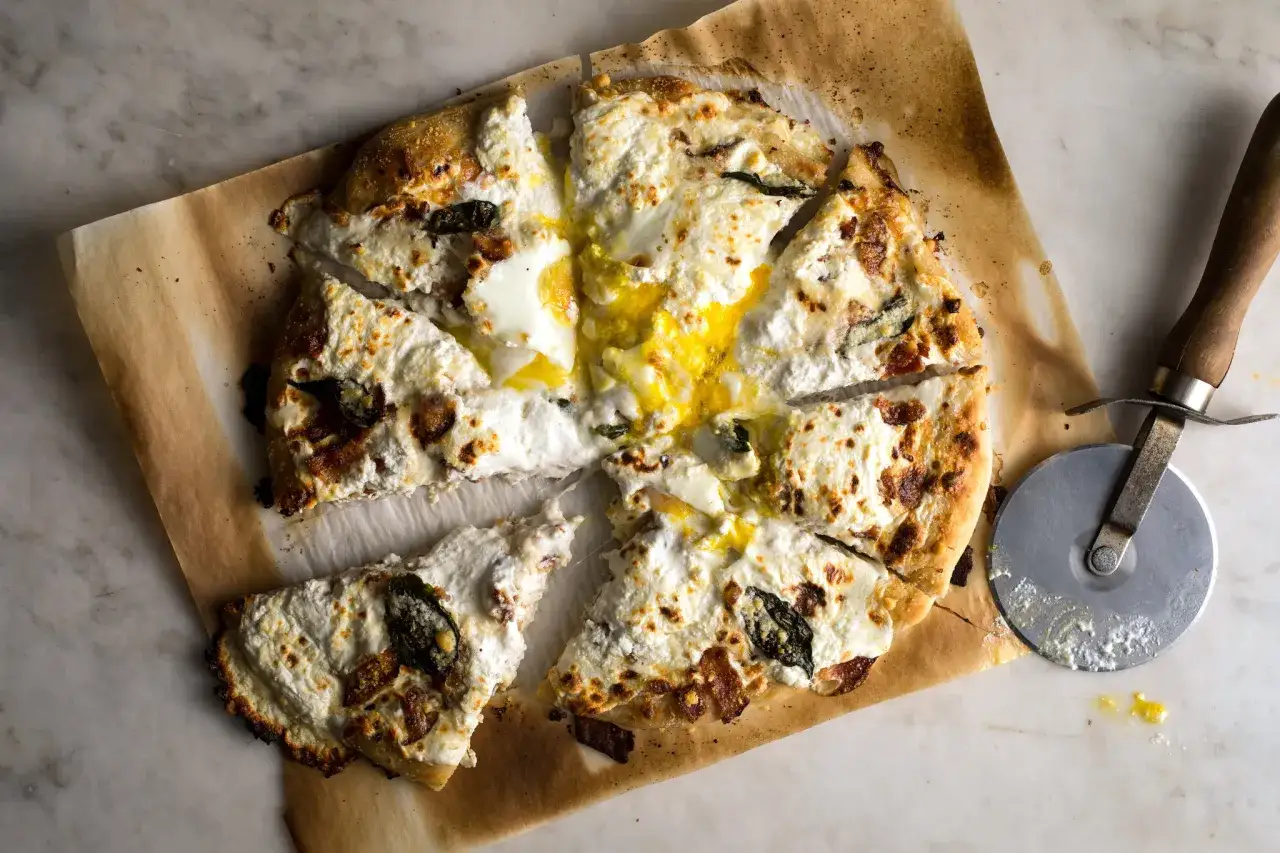 Pyszna pizza carbonara z płynnym żółtkiem i chrupiącym boczkiem, pokrojona na kawałki. Obok leży nóż do pizzy.