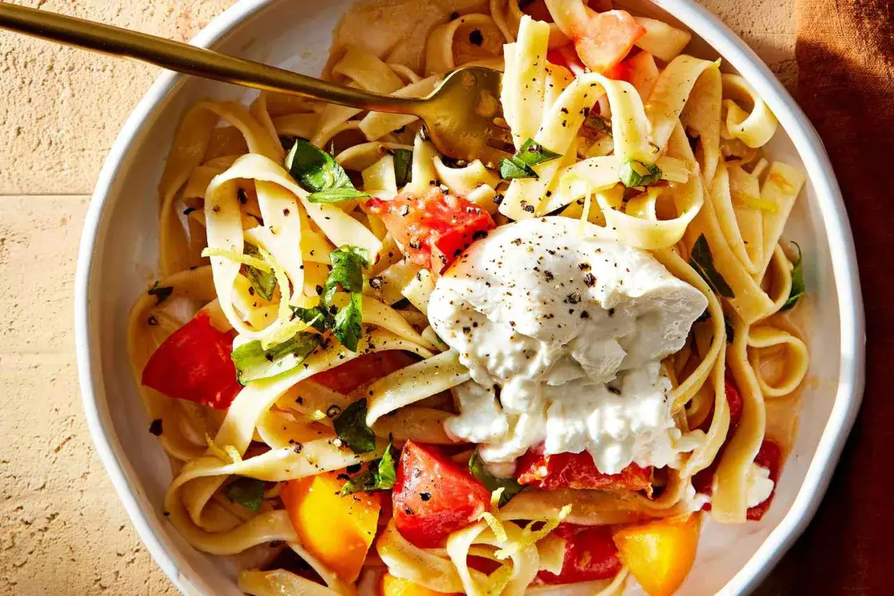 Makaron tagliatelle z pomidorami, bazylią i kremową burratą, posypany świeżo mielonym pieprzem.