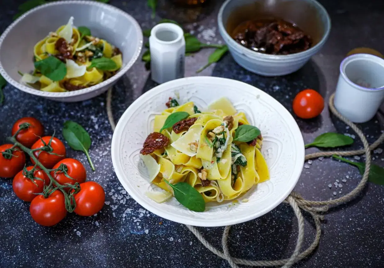 Pappardelle ze szpinakiem i suszonymi pomidorami, posypane płatkami parmezanu i orzechami. Makaron ze szpinakiem i serem pleśniowym w kremowym sosie.