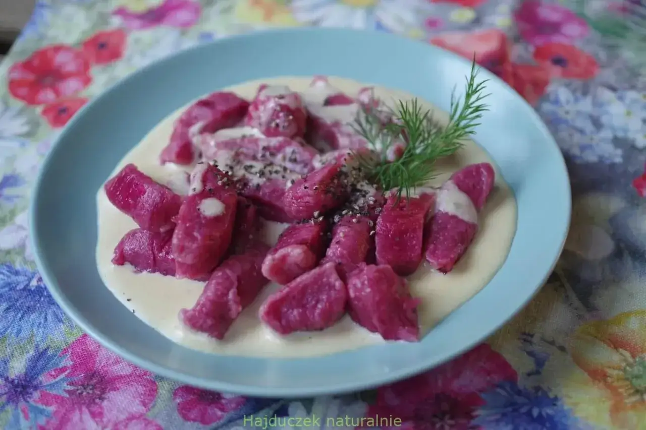 Różowe gnocchi buraczane w kremowym sosie, posypane pieprzem i udekorowane gałązką koperku.