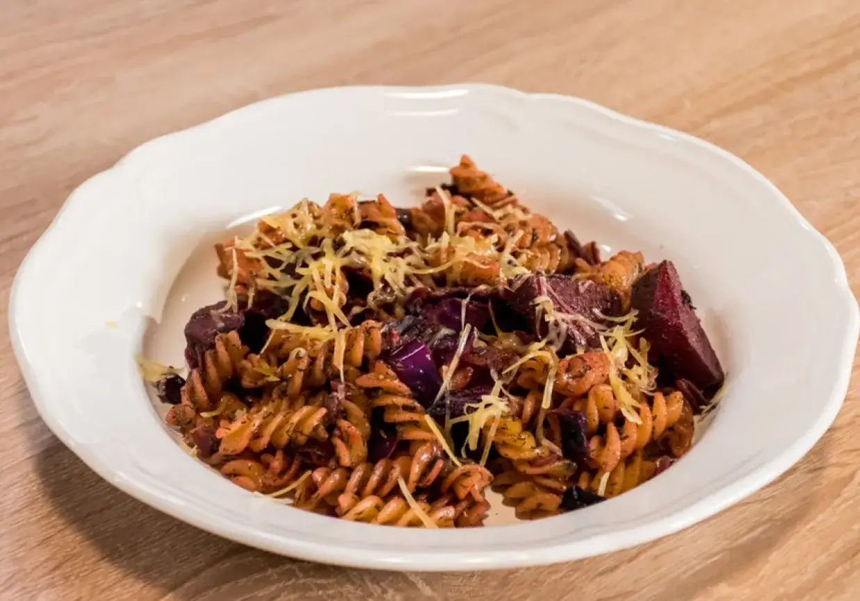 Kolorowy makaron fusilli z burakami i czerwoną kapustą, posypany startym serem.