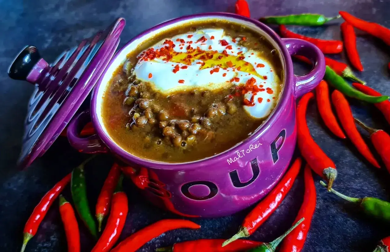 Aksamitna zupa z czarnej soczewicy w fioletowej miseczce, ozdobiona śmietaną i papryczkami chili.