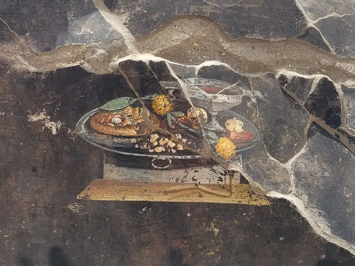 Starożytny fresk z Pompejów ukazuje ucztę, być może początki historii pizzy. Na talerzu owoce i okrągły placek.