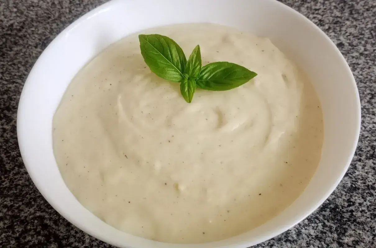 Aksamitny sos beszamelowy, idealny do zapiekanek i lasagne, ozdobiony listkiem bazylii.