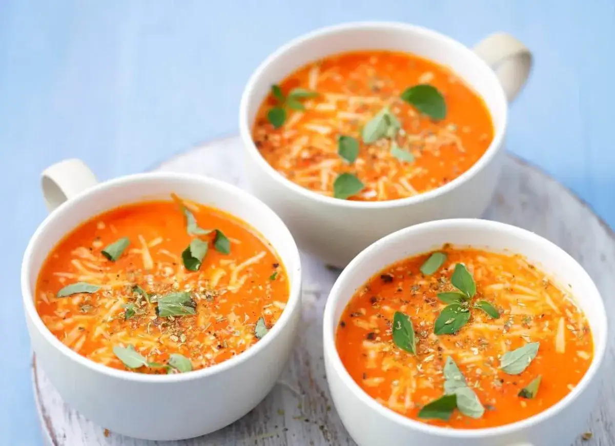 Pappa al pomodoro w trzech białych miseczkach, posypana startym serem i świeżą bazylią.