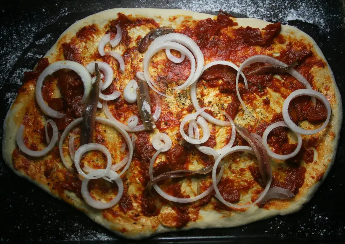 Pizza z anchois i cebulą, gotowa do pieczenia.