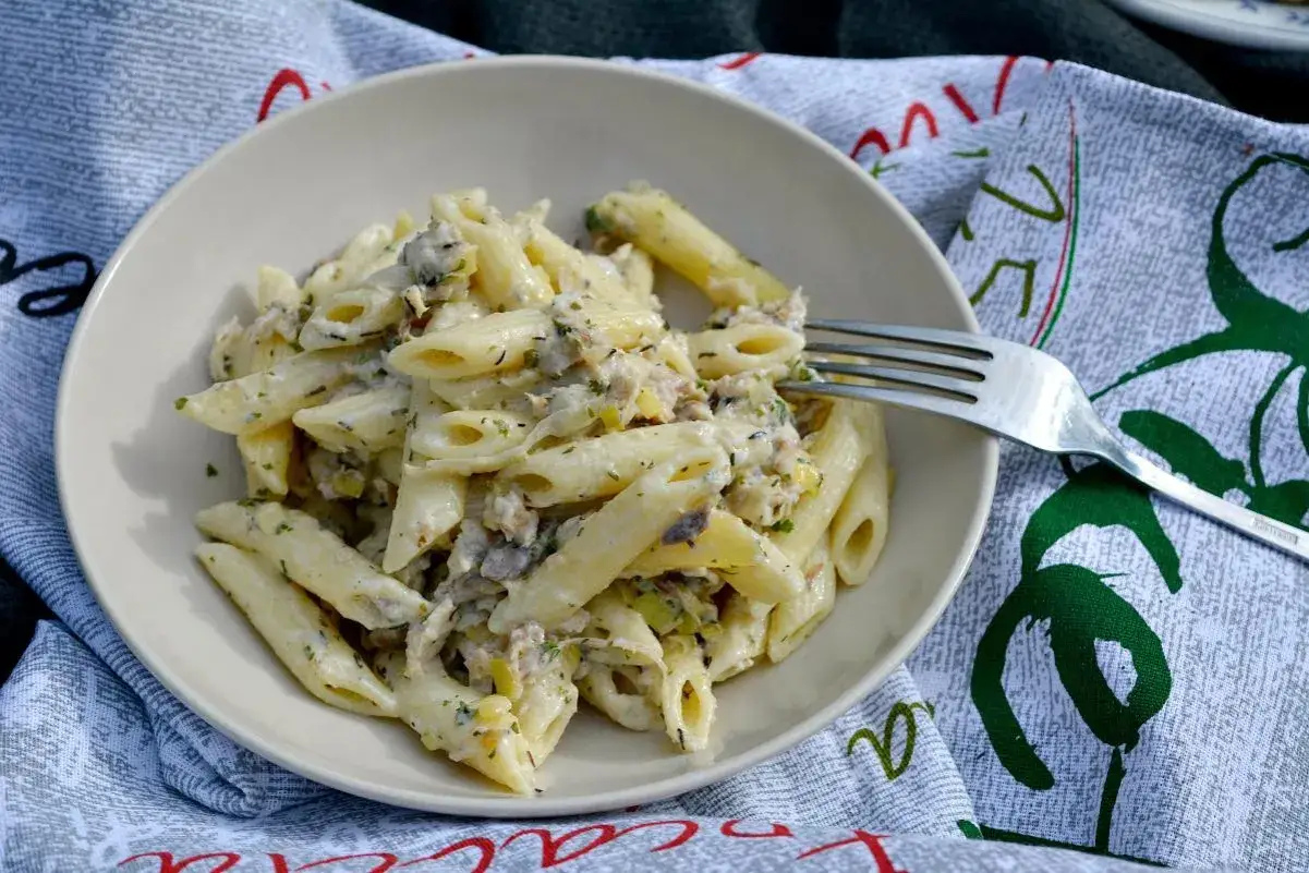 Penne z kremowym sosem i kawałkami wędzonej ryby, posypane ziołami. Idealne danie dla miłośników makaronu z wędzoną rybą.