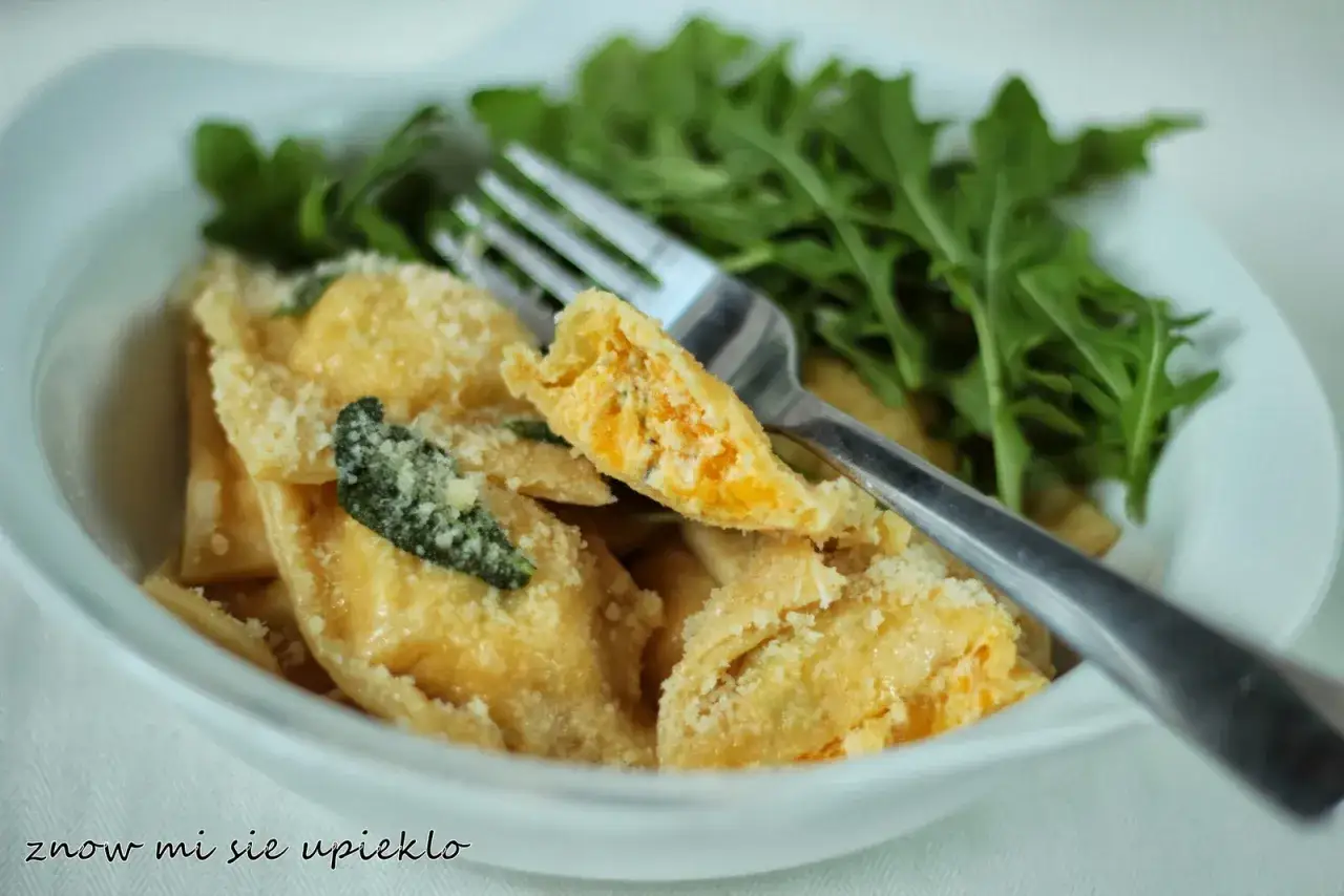 Pyszne ravioli z dynią, posypane parmezanem i udekorowane listkami szałwii, podane z rukolą.