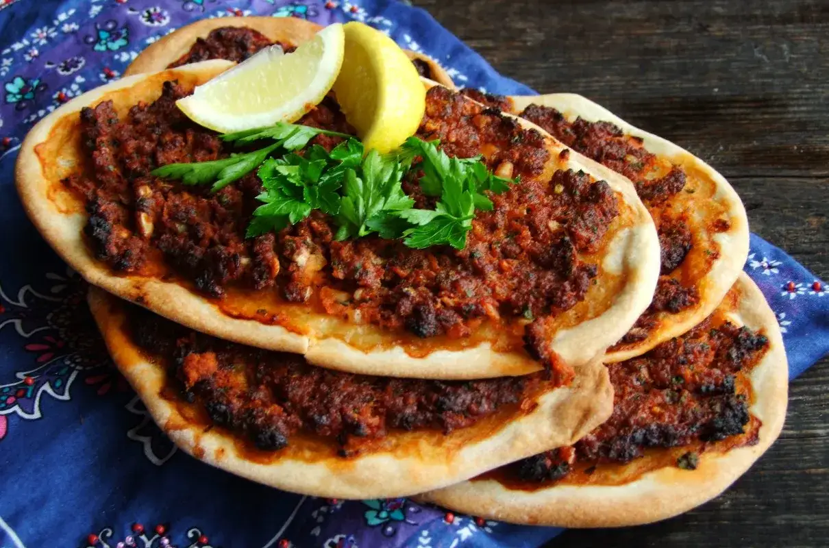 Lahmacun co to? Pyszne, cienkie placki z mięsem mielonym, pomidorami i przyprawami, ozdobione cytryną i natką pietruszki.