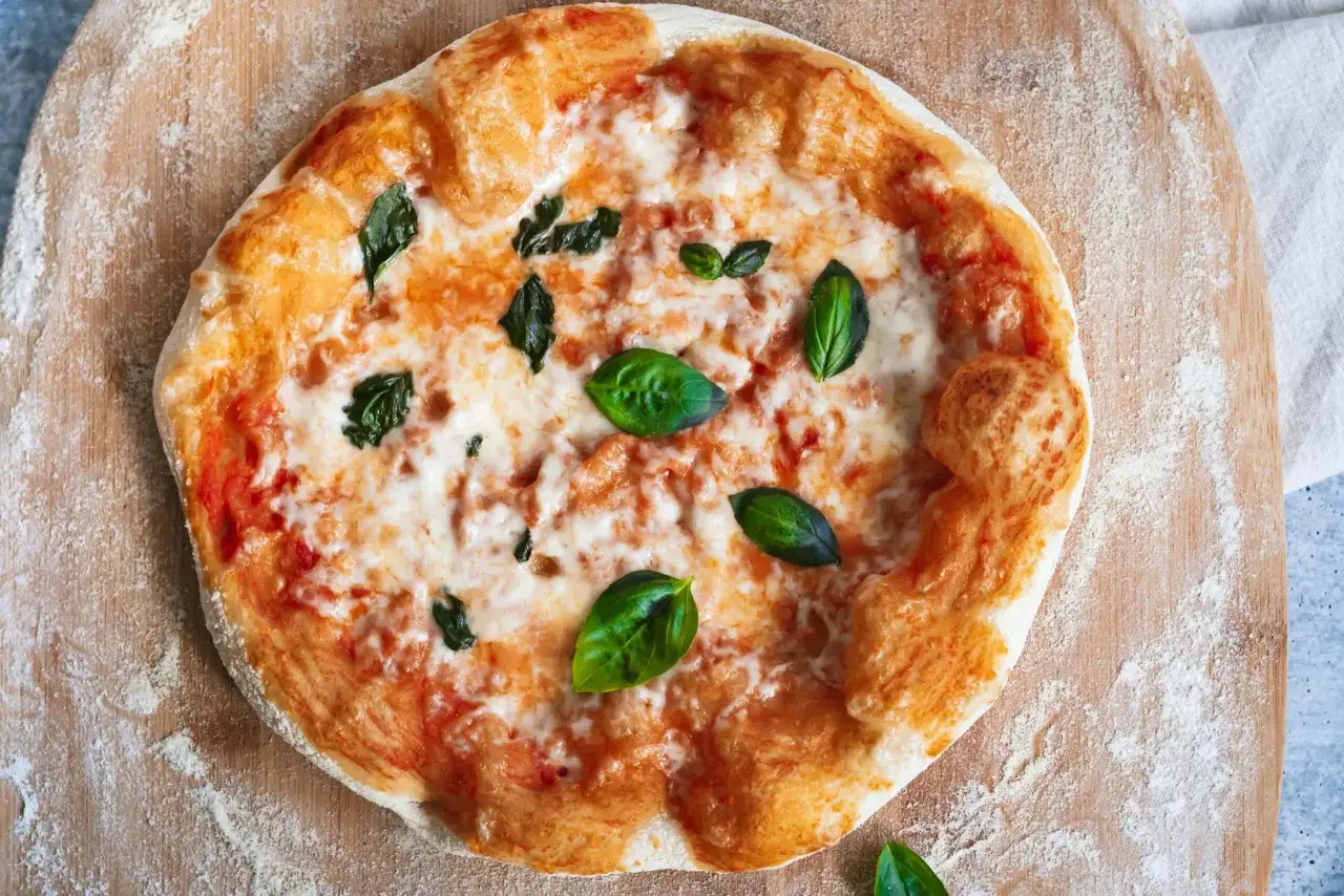 Pyszna pizza z bazylią, roztopionym serem i sosem pomidorowym, przygotowana na drewnianej desce.