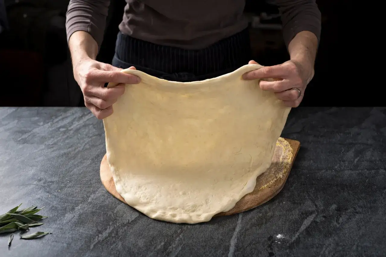 Ręce rozciągają cienkie ciasto na pizzę bez drożdży. Idealna baza na szybki obiad.