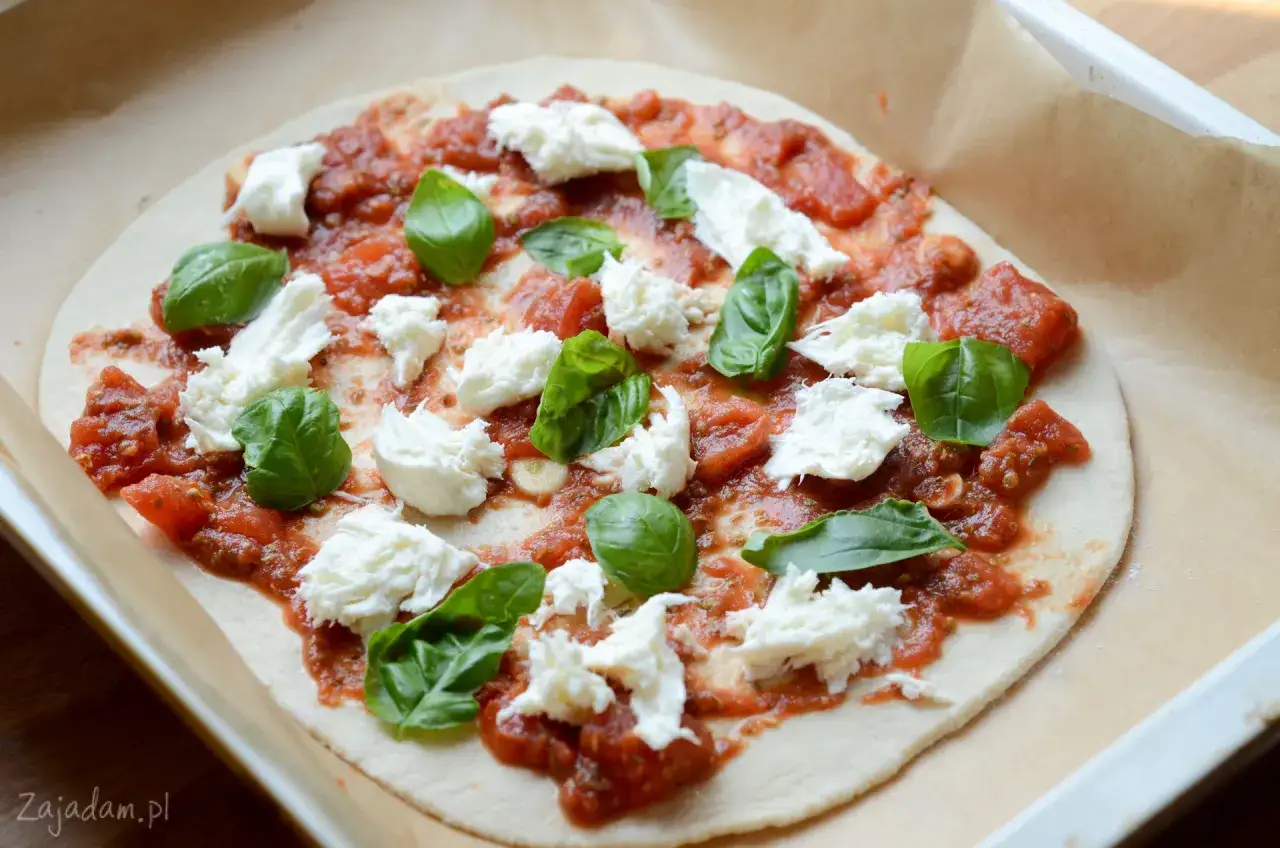 Pizza z sosem pomidorowym, świeżą bazylią i kawałkami puszystej mozzarella, gotowa do pieczenia.