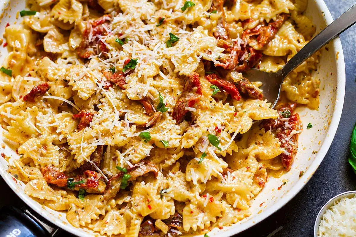Pyszny makaron farfalle z suszonymi pomidorami w kremowym sosie, posypany parmezanem i natką pietruszki.