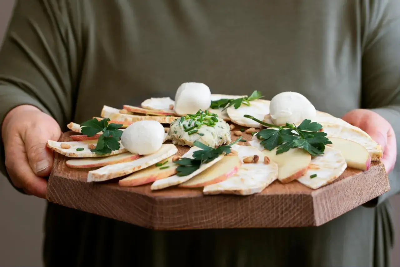 Carpaccio z selera z kulkami mozzarelli i pastą ziołową na drewnianej desce.
