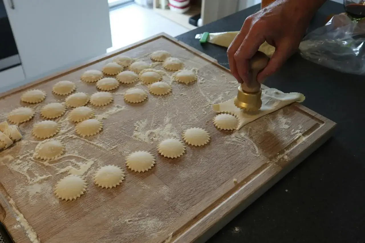 Ręcznie robione ciasto na ravioli, uformowane w gwiazdki, czeka na wypełnienie. Dłoń dociska złote narzędzie, tworząc kolejne okrągłe pierożki.