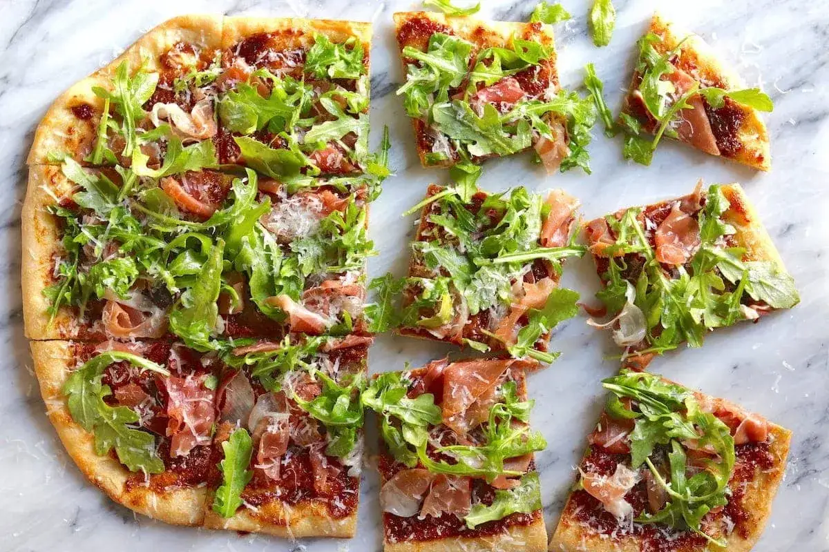 Pizza crudo z rukolą i szynką parmeńską, posypana parmezanem. Idealna na letni wieczór.