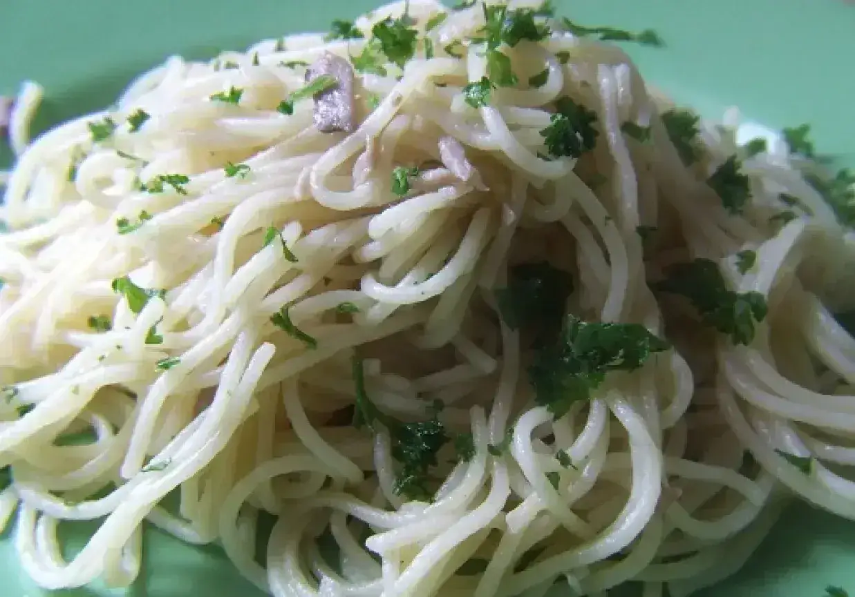 Porcja cienkiego, długiego makaronu spaghetti z posiekaną natką pietruszki na zielonym talerzu.