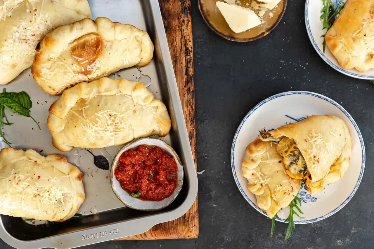 Mini calzone przepis: złociste, pieczone pierożki z serem i ziołami, podane z sosem pomidorowym i parmezanem.