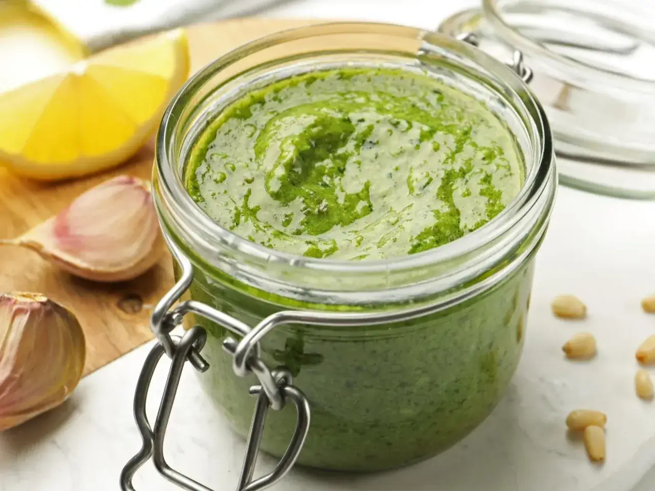 Słoik domowego, najlepszego pesto z bazylii, czosnku i orzeszków piniowych. Obok cytryna i ząbki czosnku.