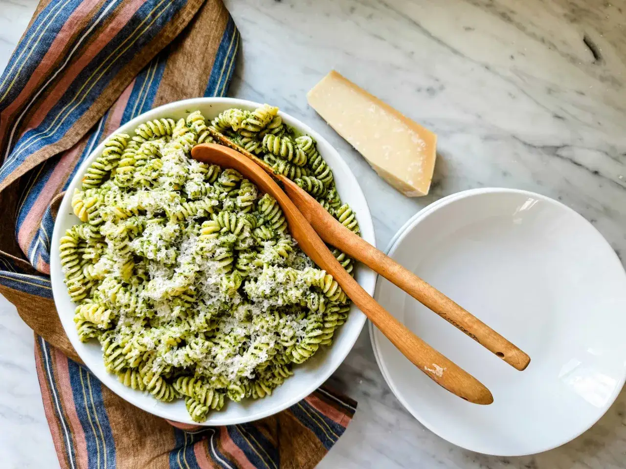Makaron z pesto, posypany startym serem. Obok kawałek sera, który może być alternatywą, jaki ser do pesto zamiast parmezanu?