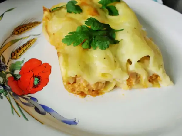 Pyszne cannelloni z mięsem mielonym, zapieczone pod serem i udekorowane natką pietruszki. Danie podane na talerzu z motywem maków i kłosów.